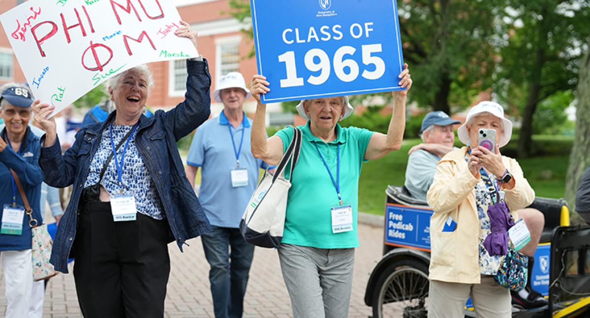 A group of alumni walk in a parade holding a sign for the Class of 1965