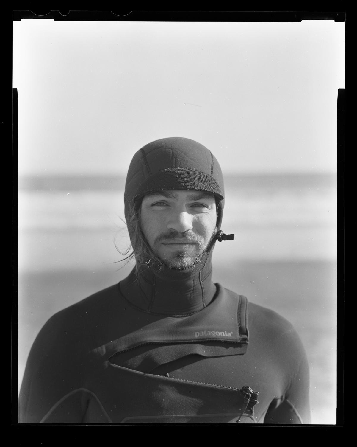 Black and white image of a man in a full body wetsuit, with only his face exposed