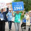 A group of alumni walk in a parade holding a sign for the Class of 1965