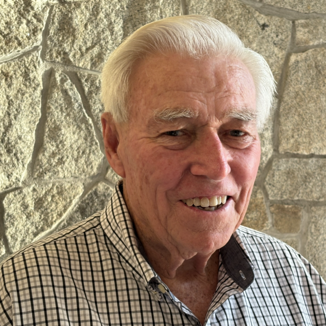 Casual outdoor headshot of an older man with white hair wearing a plaid shirt